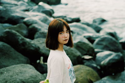 Portrait of young woman standing on rock by sea