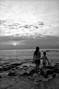 Rear view of woman with son standing on rock by sea