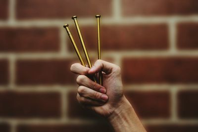 Cropped image of person holding nails against brick wall