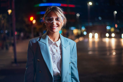 Portrait of young man wearing sunglasses standing in city at night