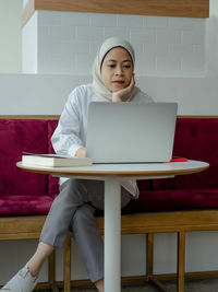 Full length of woman using phone while sitting on table