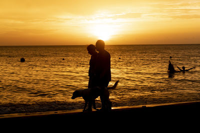 Silhouette friends standing on beach against sky during sunset