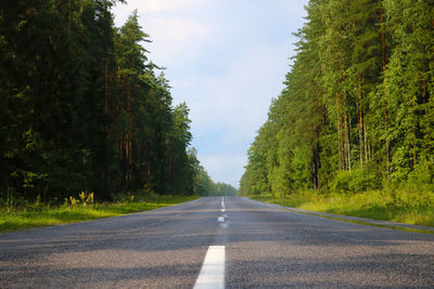 Empty road amidst trees against sky