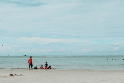 Children playing at beach against cloudy sky