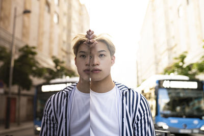 Stylish asian male model standing near building and reflecting in glass mirrored wall