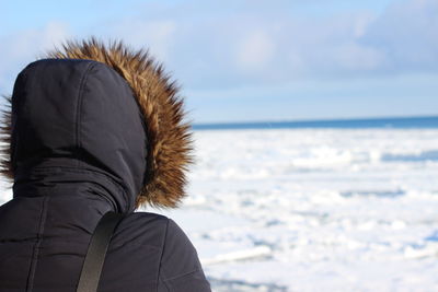 Rear view of woman wearing warm clothing standing on snow covered beach against sky
