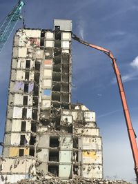 Low angle view of crane by building against sky