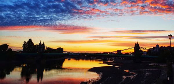 Silhouette buildings by river against sky during sunset