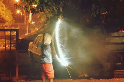 Woman standing by illuminated tree at night