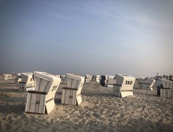 Hooded chairs on beach against sky