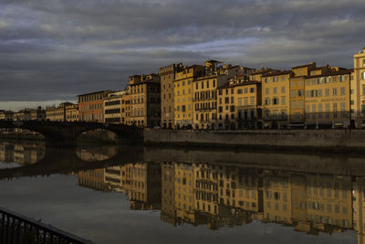 Buildings by river against sky in city at dusk