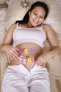 High angle view of pregnant woman with text on stomach lying on bed