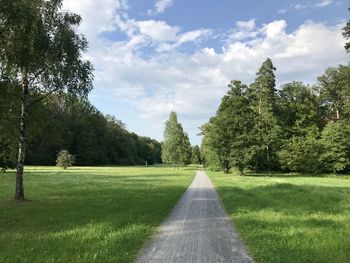 Road amidst trees on field against sky