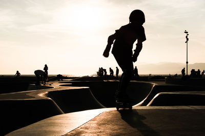 Silhouette woman skateboarding against sky at park during sunset