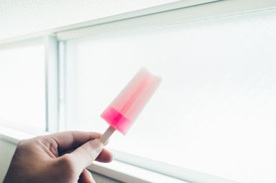 Cropped hand of woman holding flavored ice against window