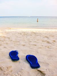 Shoes on sand at beach against clear sky