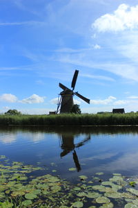 Traditional windmill by lake against sky