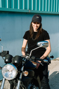 Positive female motorcyclist sitting on motorbike parked in city street on sunny day and looking at camera