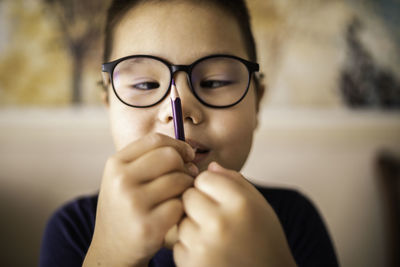 Smart young asian boy wearing glasses squints at the pencil. the vision diseases problem.