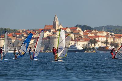 People on sea by buildings against clear sky