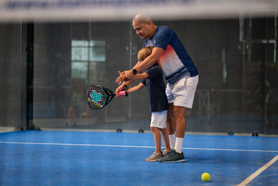 Monitor teaching padel class to child, his student - trainer teaches little boy how to play padel 