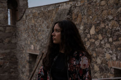 Thoughtful young woman looking away while standing against wall