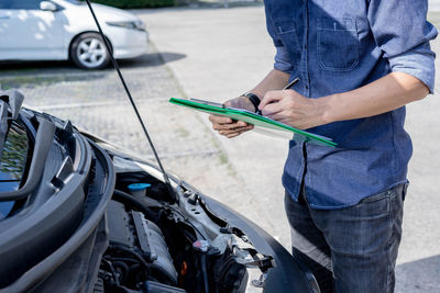 Midsection of man holding camera while standing by car