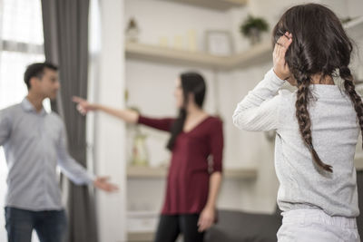 Girl covering ears while parents arguing at home