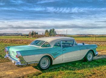 Vintage car parked by grass against sky