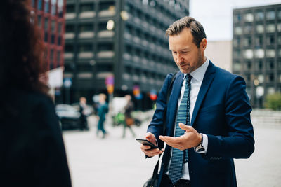 Businessman using smart phone while standing on sidewalk in city
