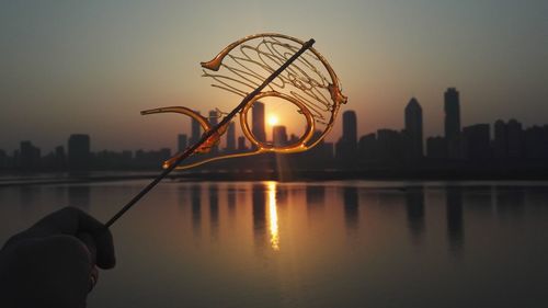 Person holding umbrella by river against sky during sunset