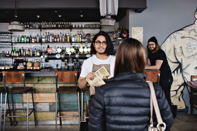 Waiter showing menu to female customer while standing at restaurant