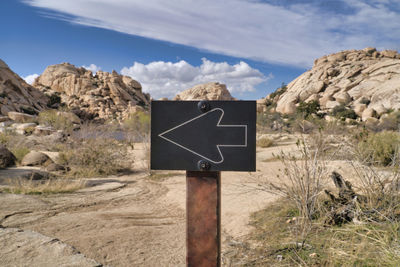 Road sign on rock against sky