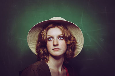 Close-up of thoughtful young woman wearing hat by blackboard