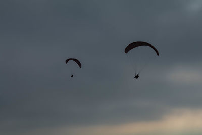 Low angle view of people paragliding against sky