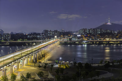 Illuminated bridge over river against sky in city at night