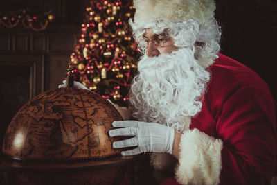 Man wearing santa claus costume looking at globe at home