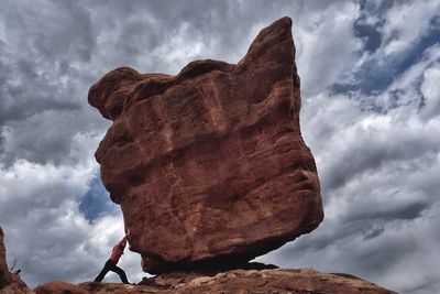 Low angle view of woman pushing boulder rock against cloudy sky