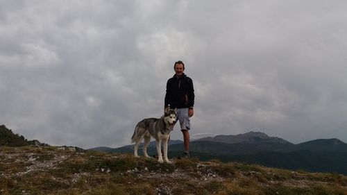 Portrait of man with dog standing on mountain against sky