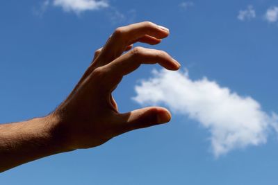 Low angle view of cropped hand against blue sky