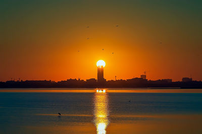 Silhouette birds flying over lake against sky during sunset