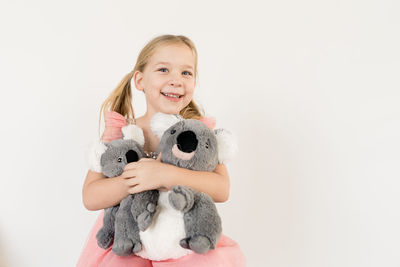 Cute blond little girl hugging koala stuffed animals indoors