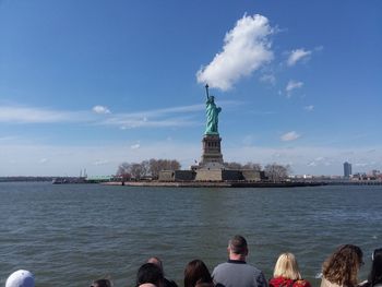 Statue of people at waterfront against cloudy sky