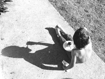 High angle view of shirtless boy eating cake while sitting on footpath by field