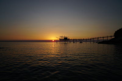 Silhouette built structure over sea against sky during sunset