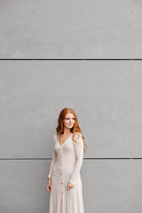 Portrait of young woman standing against wall