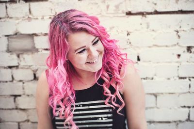 Portrait of beautiful young woman standing against brick wall