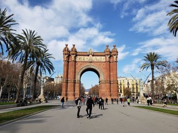 People walking in front of historical building against cloudy sky