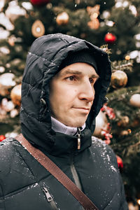 A young man warmly dressed on the street against the background of christmas  on a snowy cold day.