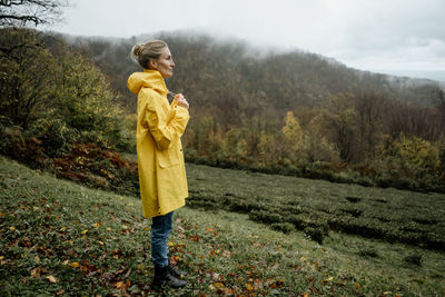 Middle aged woman in yellow raincoat walking in rainy weather in the countryside